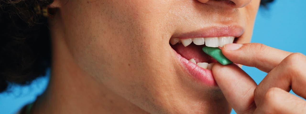 A close-up photo of a person putting a piece of gum into their mouth